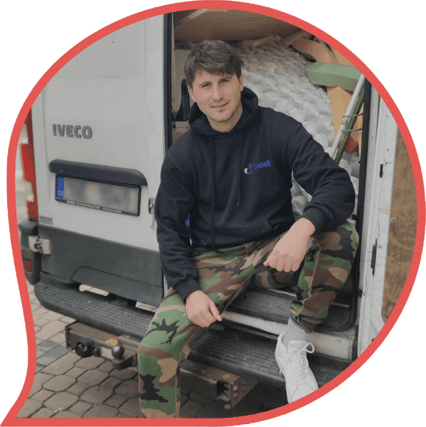 Muž v montérkách sedící na zadních dveřích vyklízecího vozu připravený k odvozu nepotřebných věcí při vyklízení nemovitosti.