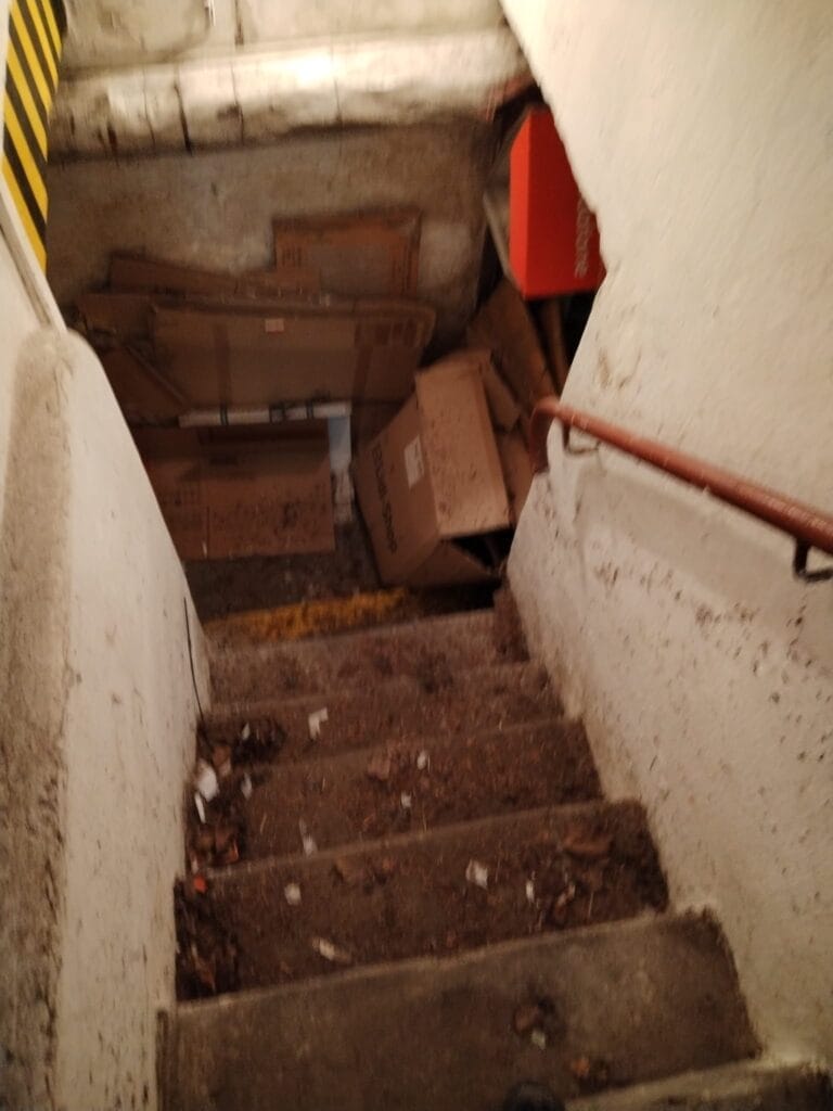 Špinavé schodiště s odpadky a kartonovými krabicemi, zanedbaný prostor pro vyklízení